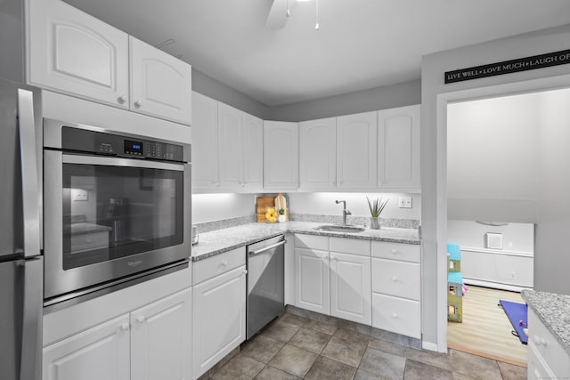 kitchen featuring appliances with stainless steel finishes, a sink, white cabinetry, and light stone countertops