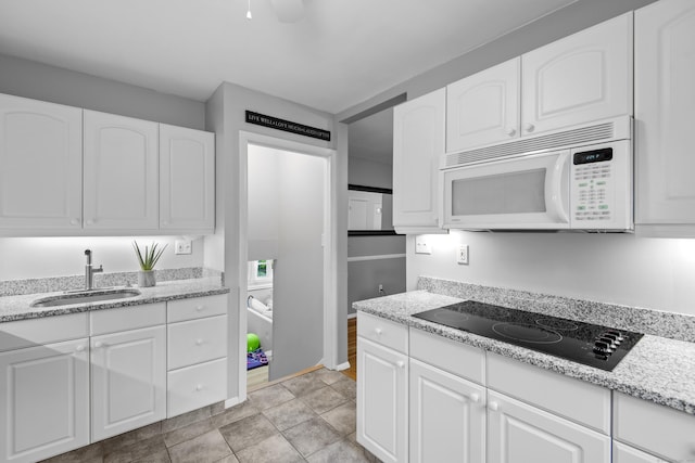 kitchen with white microwave, a sink, black electric stovetop, and white cabinetry