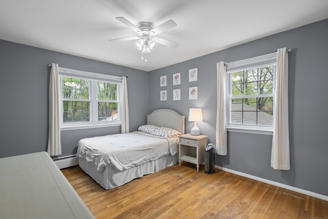 bedroom with hardwood / wood-style flooring, a baseboard heating unit, ceiling fan, and baseboards