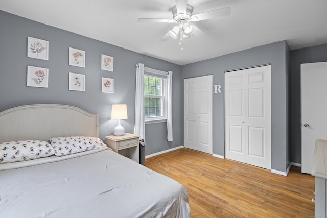 bedroom featuring two closets, light wood finished floors, baseboards, and ceiling fan