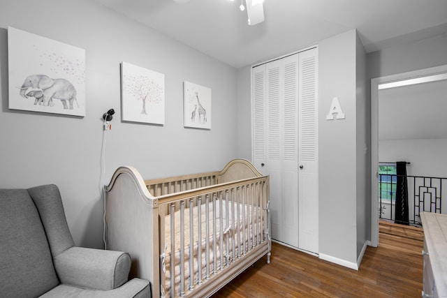 bedroom with wood finished floors, a closet, baseboards, a crib, and ceiling fan