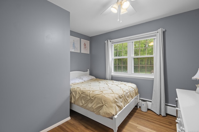 bedroom with wood finished floors, baseboard heating, a ceiling fan, and baseboards