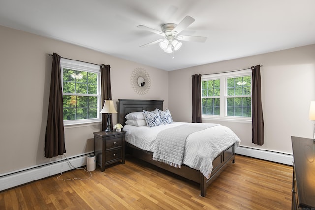 bedroom with a baseboard heating unit, multiple windows, and light wood-style floors