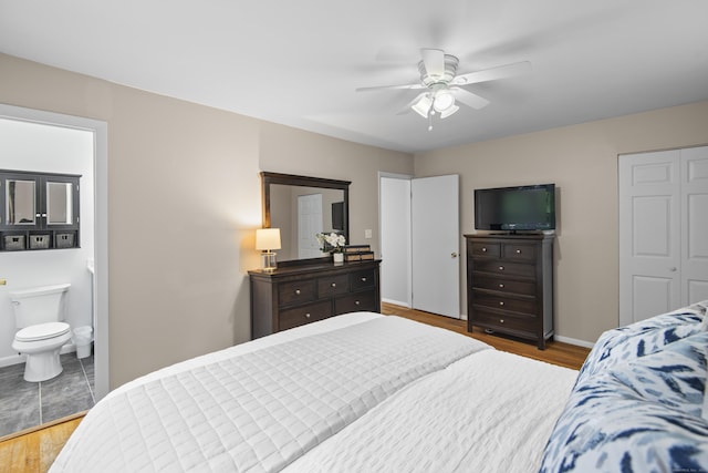 bedroom featuring wood finished floors, baseboards, ensuite bath, and a ceiling fan