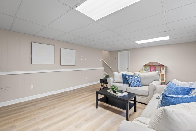 living area featuring wood finished floors, a paneled ceiling, baseboards, and stairs