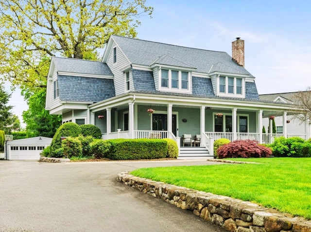 view of front of house with a chimney, a front yard, covered porch, and a detached garage