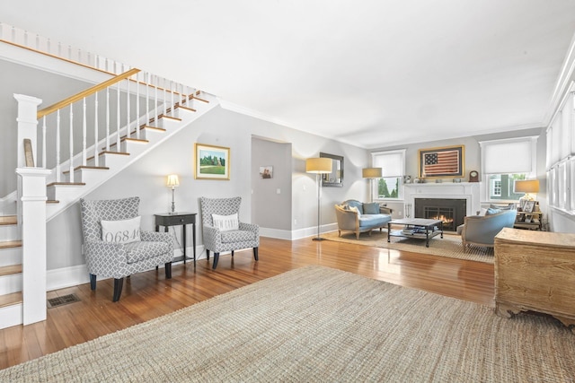 living room featuring stairway, crown molding, a warm lit fireplace, and wood finished floors