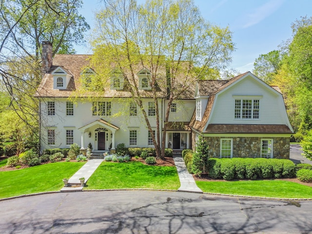 view of front of house featuring a front lawn, a gambrel roof, a chimney, and stone siding