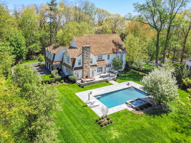 back of house featuring a yard, stone siding, and a chimney
