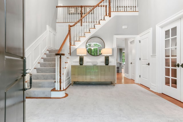 stairs featuring a wainscoted wall, wood finished floors, a decorative wall, and a towering ceiling