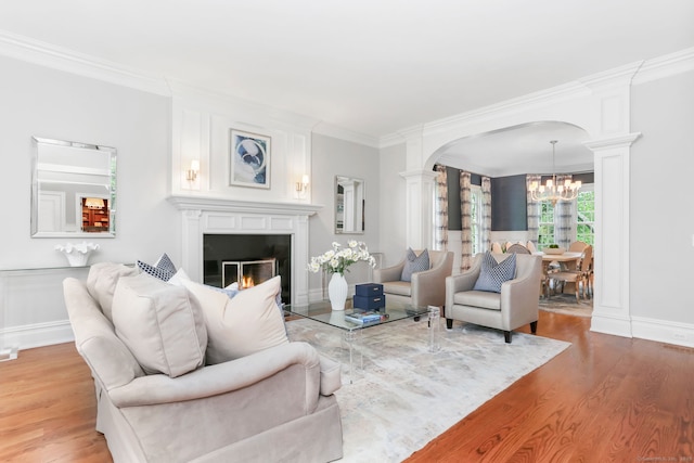 living room featuring ornamental molding, a chandelier, wood finished floors, and ornate columns