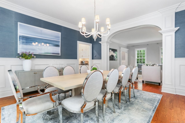 dining room with decorative columns, a decorative wall, a wainscoted wall, wood finished floors, and arched walkways