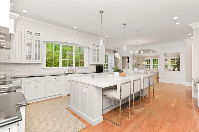 kitchen featuring tasteful backsplash, decorative columns, a kitchen breakfast bar, light wood finished floors, and white cabinets