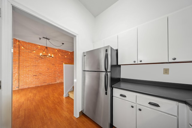 kitchen with dark countertops, freestanding refrigerator, brick wall, and white cabinetry