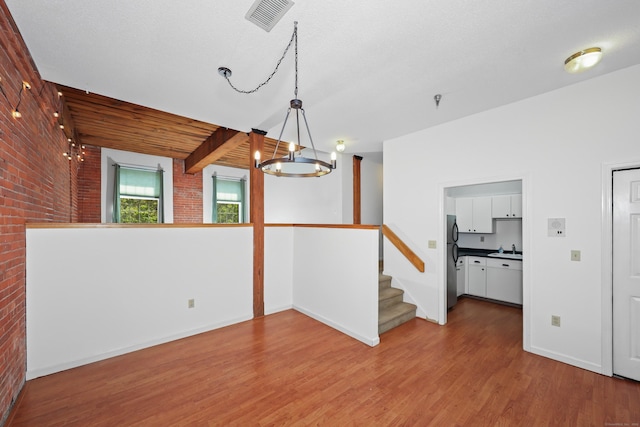 interior space with brick wall, visible vents, wood finished floors, baseboards, and a notable chandelier