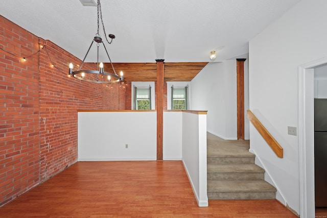 interior space featuring baseboards, brick wall, a notable chandelier, and wood finished floors