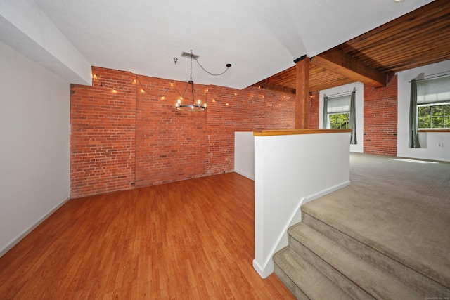 interior space featuring brick wall, wood finished floors, baseboards, beamed ceiling, and a chandelier