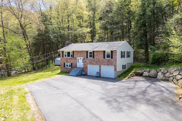 split foyer home with brick siding, a wooded view, a chimney, and aphalt driveway