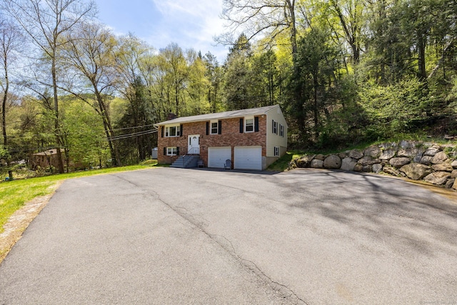 split foyer home with brick siding, a garage, a view of trees, and aphalt driveway