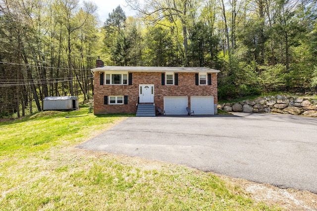 raised ranch with a front lawn, brick siding, a chimney, driveway, and a wooded view