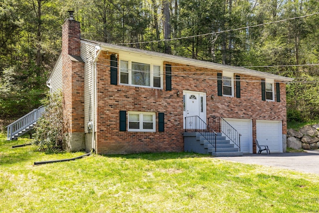 raised ranch featuring a garage, a chimney, a front yard, and aphalt driveway