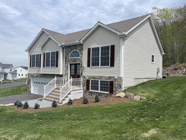 raised ranch featuring french doors, a front yard, a garage, aphalt driveway, and stone siding