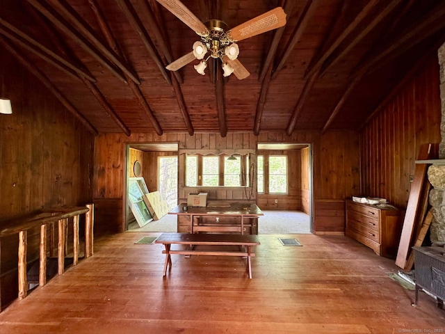 interior space with wood walls, lofted ceiling with beams, hardwood / wood-style floors, wooden ceiling, and ceiling fan
