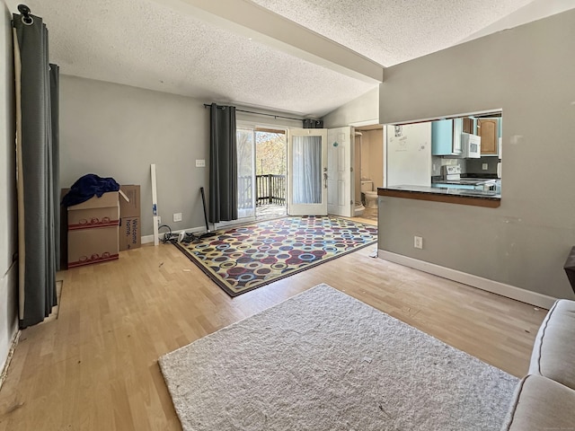 living area featuring a textured ceiling, baseboards, light wood-style flooring, and lofted ceiling