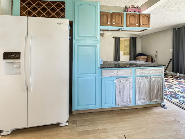 kitchen featuring a peninsula, light wood-style flooring, dark stone counters, a textured ceiling, and white refrigerator with ice dispenser