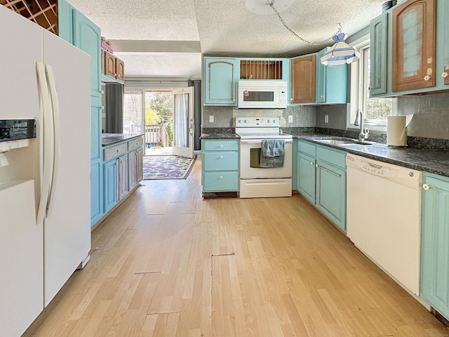 kitchen with dark countertops, a sink, white appliances, a textured ceiling, and light wood-style flooring