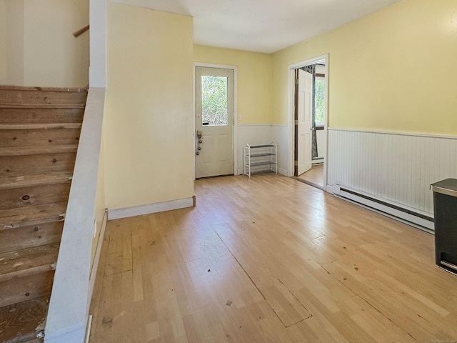 spare room featuring a healthy amount of sunlight, stairway, a baseboard heating unit, and wood finished floors