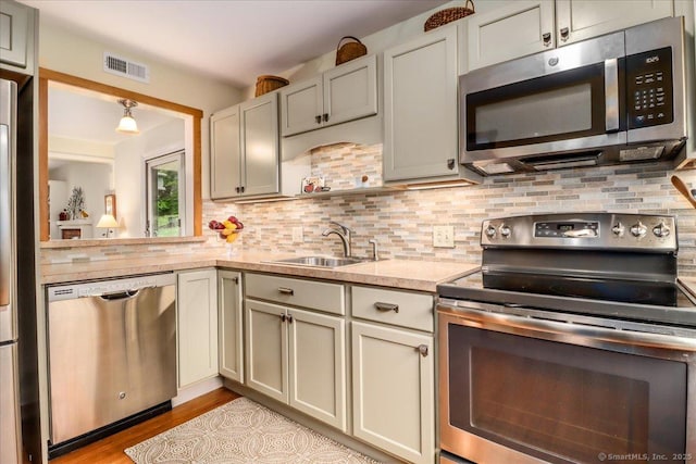 kitchen featuring stainless steel appliances, light countertops, a sink, decorative backsplash, and light wood finished floors