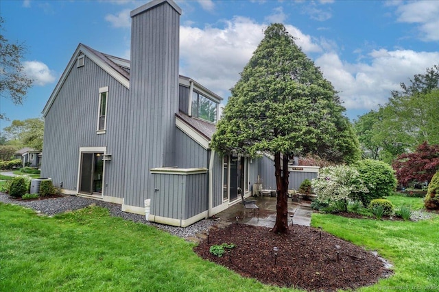 rear view of property with a lawn, a patio, a chimney, and central air condition unit