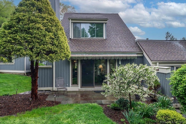 rear view of property featuring roof with shingles, a patio area, a yard, and board and batten siding