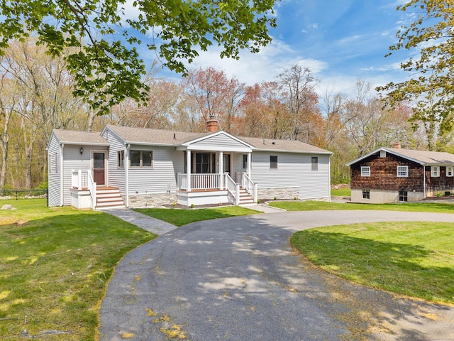view of front of property featuring a front lawn, curved driveway, a chimney, a shingled roof, and a porch