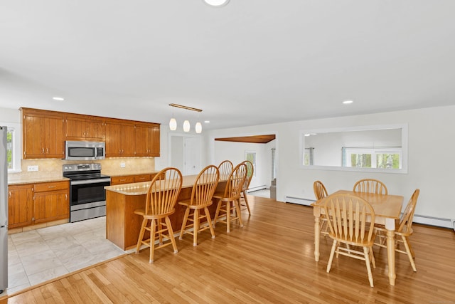 7 Old Black Point Rd, East Lyme, CT 06357 - kitchen featuring appliances with stainless steel finishes, backsplash, light wood-type flooring, a kitchen bar, and brown cabinets