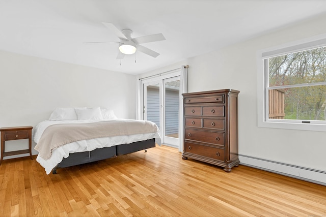 bedroom featuring a ceiling fan, a baseboard heating unit, multiple windows, and light wood finished floors
