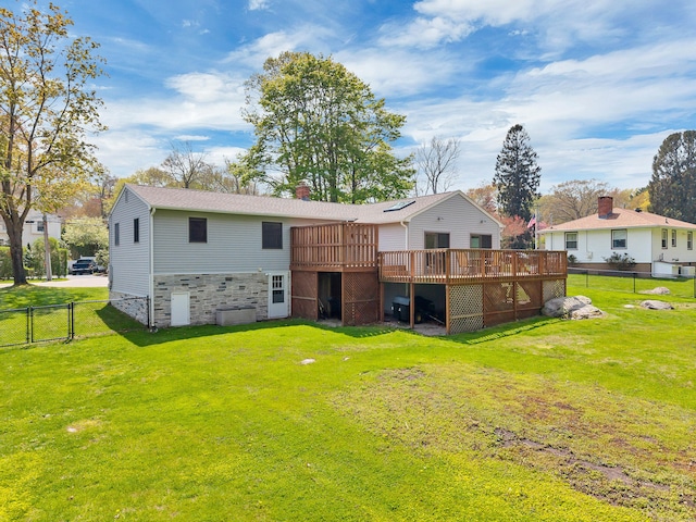 rear view of property with a wooden deck, fence, stone siding, a gate, and a lawn