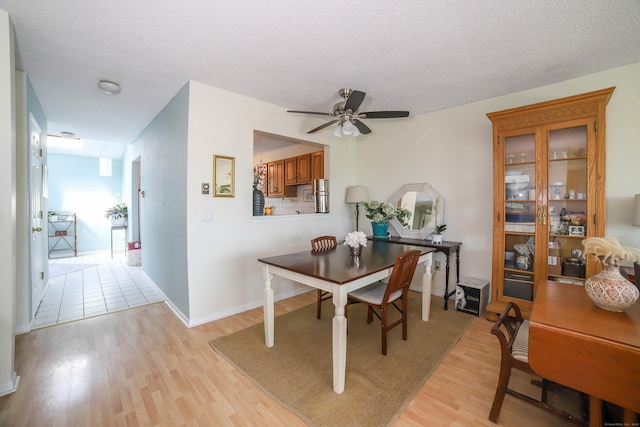 dining space featuring light wood finished floors, a textured ceiling, baseboards, and ceiling fan