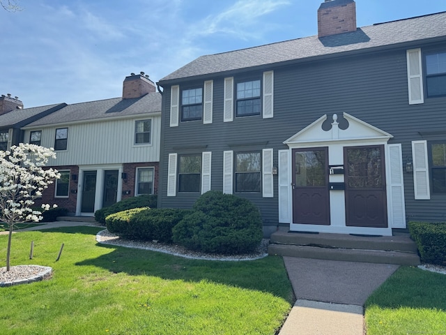 multi unit property featuring roof with shingles, a chimney, brick siding, and a front yard