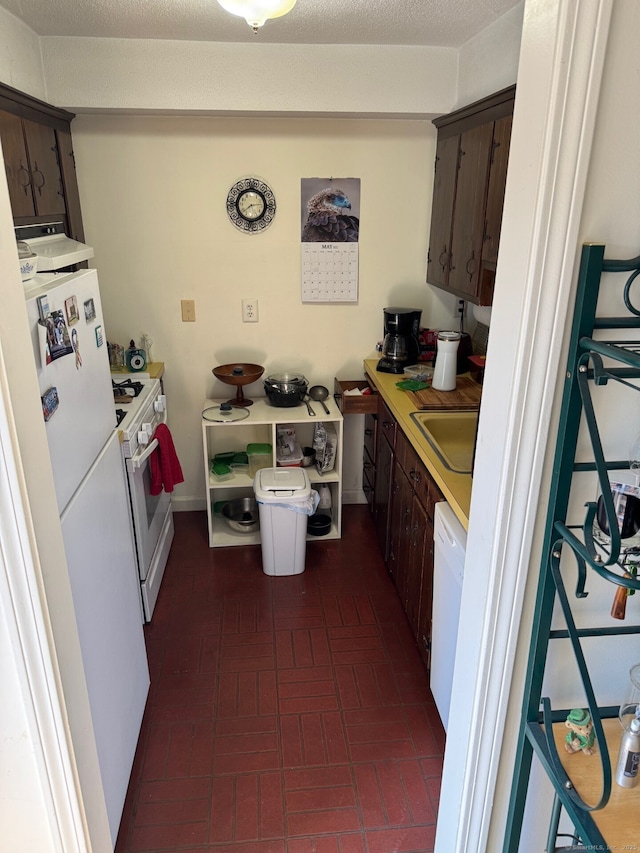 kitchen with a sink, dark brown cabinets, brick patterned floor, and white appliances