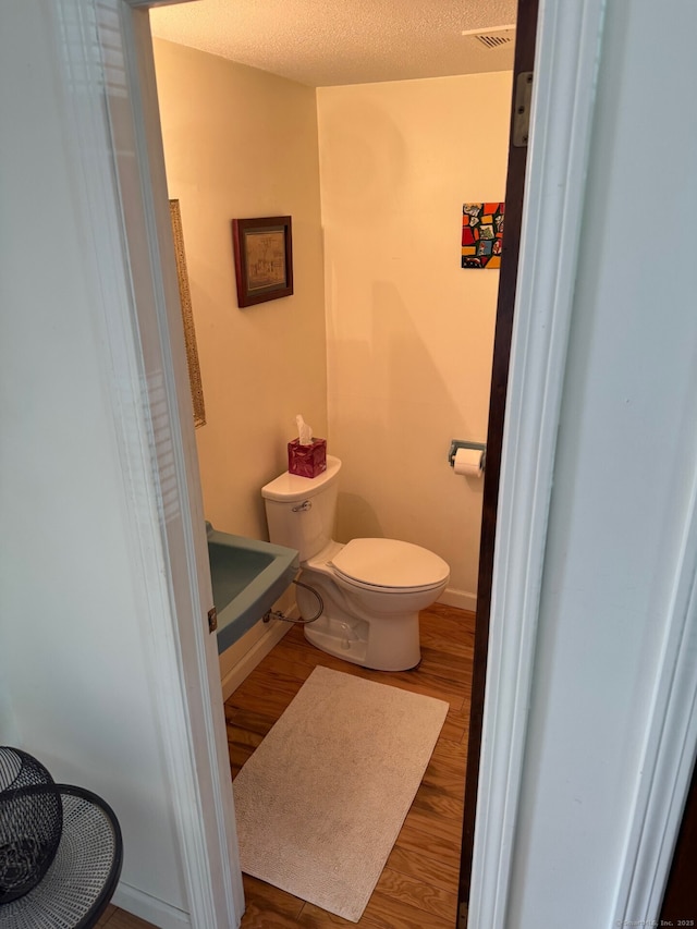 bathroom with a textured ceiling, visible vents, wood finished floors, baseboards, and toilet