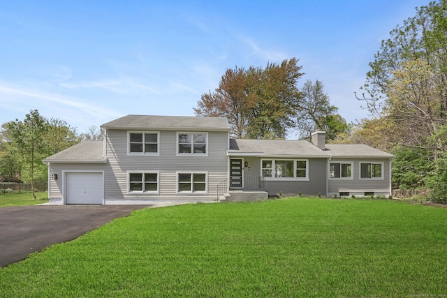 split level home featuring a garage, a chimney, driveway, a front yard, and a shingled roof