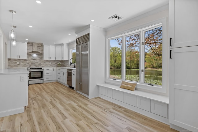 kitchen with stainless steel appliances, wall chimney range hood, tasteful backsplash, light countertops, and white cabinetry