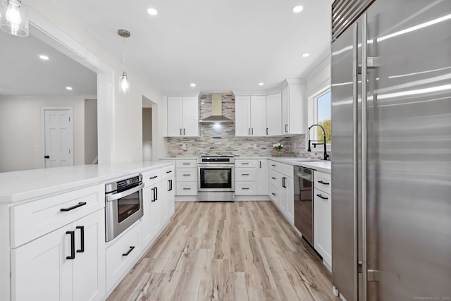 kitchen with stainless steel appliances, wall chimney exhaust hood, tasteful backsplash, light countertops, and light wood-type flooring