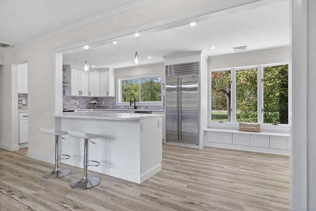 kitchen featuring built in refrigerator, ornamental molding, light countertops, white cabinetry, and light wood-style flooring