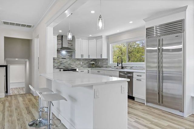 kitchen with appliances with stainless steel finishes, wall chimney exhaust hood, a sink, light wood-type flooring, and crown molding