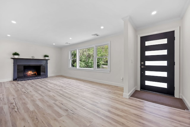 unfurnished living room featuring ornamental molding, light wood finished floors, baseboards, recessed lighting, and a glass covered fireplace