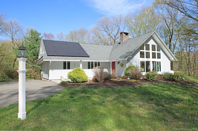 view of front of house featuring a shingled roof, a chimney, solar panels, and a front yard