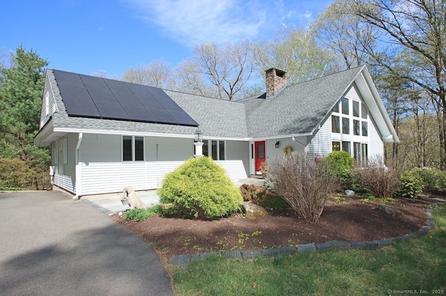 view of front of property featuring roof mounted solar panels, covered porch, a shingled roof, and a chimney